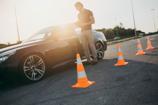 Driving School Or Test. Beautiful Young Woman With Instructor Learning How To Drive And Park Car Between Cones.