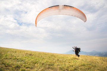 A man paraglider taking off from the edge of the mountain with fields in the background....