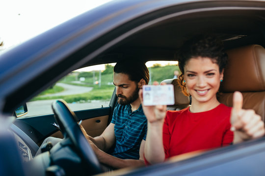 Driving school. Beautiful young woman successfully passed driving school test. She is sitting in car, looking at camera and holding driving license in hand.