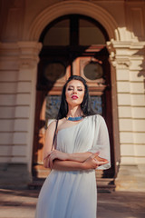 Beautiful woman wearing white wedding dress, accessories and jewellery on ancient architecture background outdoors.