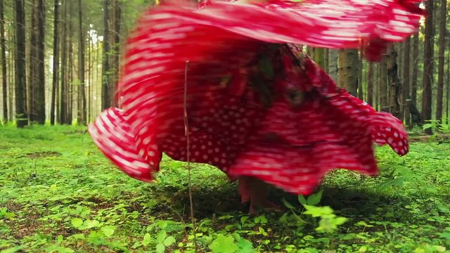 barefooted woman in a bright gypsy dress whirls in a dance in the forest.