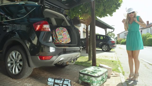 LENS FLARE: Lighthearted young woman fails to close the trunk of her black car and her suitcases fall all over the driveway. Female tourist fails to catch travel bags falling from the back of SUV.