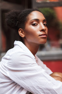Portrait of beautiful african girl with dark curly hair in white shirt thoughtfully looking in camera