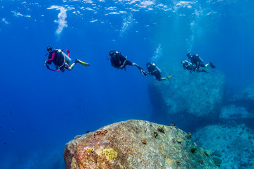 Fototapeta na wymiar SCUBA divers swimming over a shallow water, rocky reef