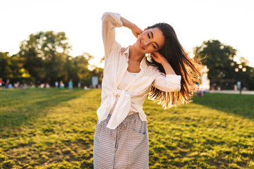 Obraz premium Pretty smiling girl in white shirt joyfully looking aside while dancing in city park