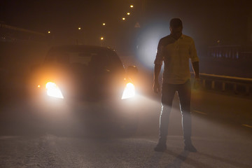 Incident on the road. Unknown person stands in the middle of the roadway at night in the fog by the...