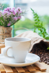 White cup of black coffee or tea on wooden plate over blurred coffee bean with nature sun lighting.