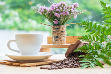 White cup of black coffee or tea on wooden plate over blurred coffee bean with nature sun lighting.