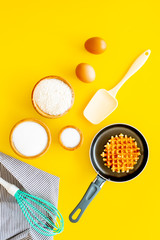 Ingredients for belgian waffles. Eggs, flour, sugar near waffle on pan, whisk for whipping on yellow background top view copy space