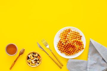 Hot round waffles ready to eat. Belgian recipe. Waffles on plate near honey and dried fruits on yellow background top view copy space