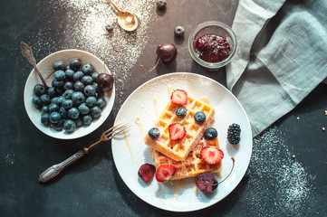 Waffles with berries on black background, top view flat lay