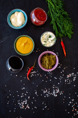 Ingredients for dishes. Dip sause, dressing. Ketchup, mayonnaise, mustard, soy sauce, barbecue sauce, pesto, mustard, sour near chili pepper and greenery on black background top view