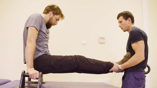 Doctor physiotherapist helping young disable man to do the exercise at the rehabilitation clinic