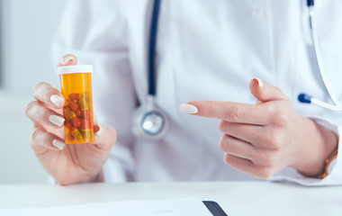 Young female medicine doctor sitting in front of working table holding jar of pills and explains to the patient how to take medication. Medical and pharmacy concept