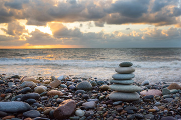 Pyramid of stones from pebble for meditation, on a background a seashore at sunset a sun. Marine background