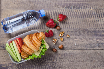 Back to school concept. Lunch box with croissant, fruits and vegetables on wooden background. Copy space, top view