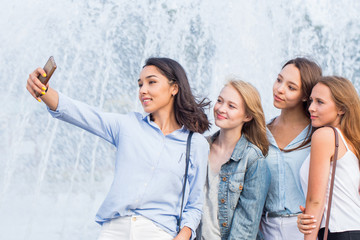 A group of young attractive girls of students makes a selfie on the background of a beautiful fountain