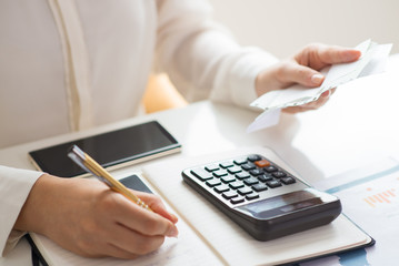 Closeup of person holding bills and calculating them. Notebook, calculator and smartphone lying on...