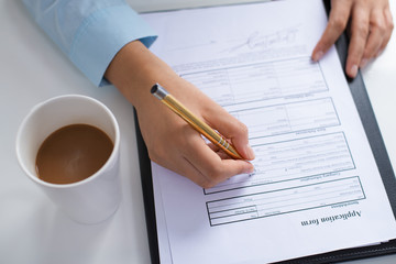 Closeup of person making notes in filled application form. Entrepreneur sitting at desk with coffee cup. Paperwork and recruitment concept. Cropped view.