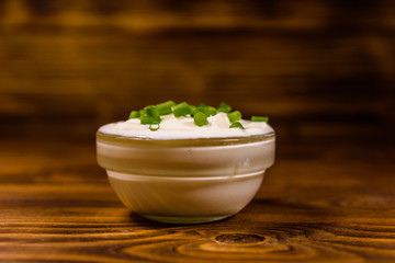 Glass bowl with sour cream and chopped green onion on wooden table