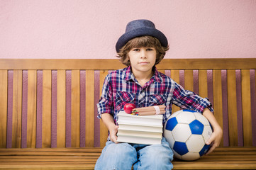 Little boy holding stack of books and a foot ball ready to go back to school.