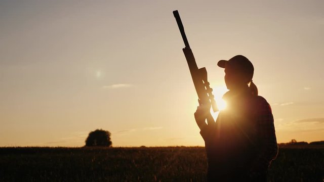Silhouette of a woman with a sniper rifle. Standing in the rays of the setting sun