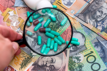 Hand with magnifier above green pills on australian dollars