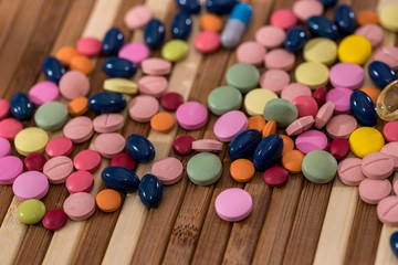 Pills of different colors dispersed on wooden background