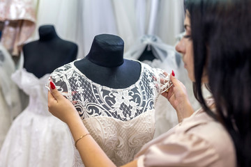 Seller in wedding salon correcting dress on mannequin