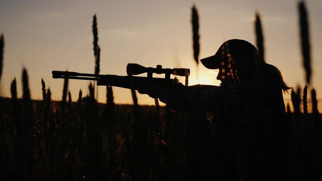 The hunter is hiding in thickets, aiming from a rifle with an optical sight