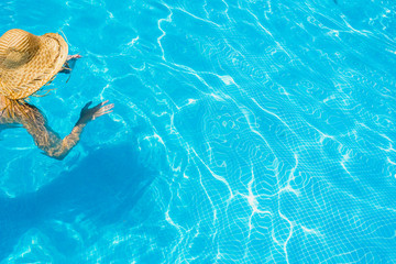 Woman in a pool with hat relaxed and rested.