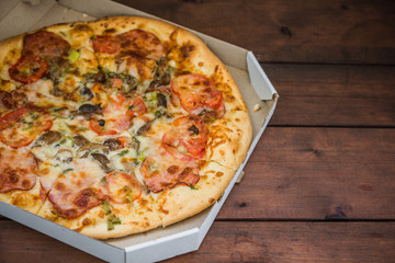 Pizza on wooden boards in rustic style. Italian pizza in a cardboard box. Simple food on a wooden background. Tasty dish for lunch