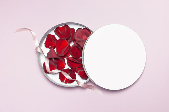 Round white cardboard blank box with red rose petals top view flat lay. Mock up on pink background. Packaging design, an empty box for shopping.