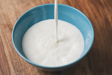 Close-up pour fresh milk into blue bowl on wood table