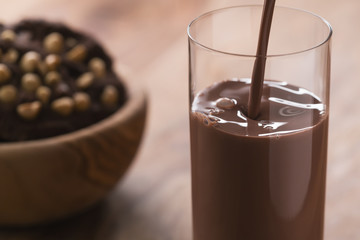 Close-up pour chocolate milk into glass on wood table with cookies on background