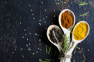 White spoons with spices are on a black wooden table