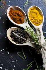 White spoons with spices are on a black wooden table