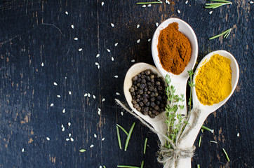 White spoons with spices are on a black wooden table