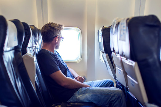 Passenger traveler looking at window in airplane, travel by flight, man tourist sitting in air plane