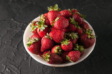 Fresh strawberries in a plate on a black background.