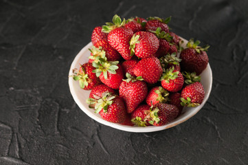 Fresh strawberries in a plate on a black background.
