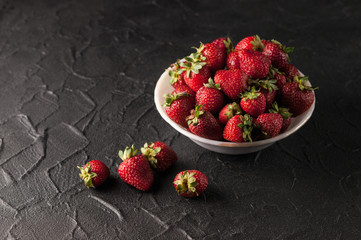 Fresh strawberries in a plate on a black background.