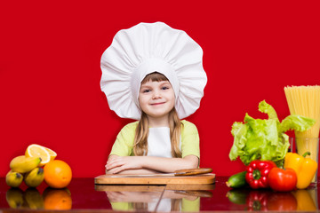 Happy little girl in chef uniform cuts fruit in kitchen. Kid chef. Cooking Process Concept