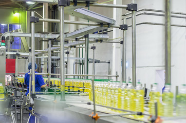 line of food production of refined sunflower oil. Woman worker at a factory on a conveyor background with bottles of vegetable oil.