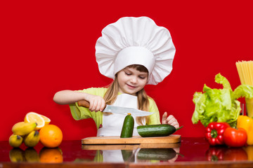 Happy little girl in chef uniform cuts vegetables in kitchen. Kid chef. Vegetarian. Cooking Process Concept
