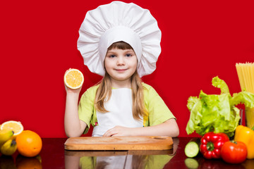 Happy little girl in chef uniform cuts fruit in kitchen. Kid chef. Cooking Process Concept