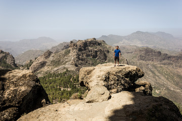 Young man standing on rock top on sunny day in Roque Nublo, Gran Canaria. Hiker on mountain edge in Canary Islands, Spain. Outdoor activity, adventure, explore, freedom concepts