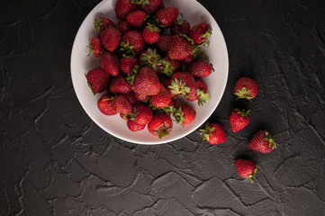 Fresh strawberries in a plate on a black background.