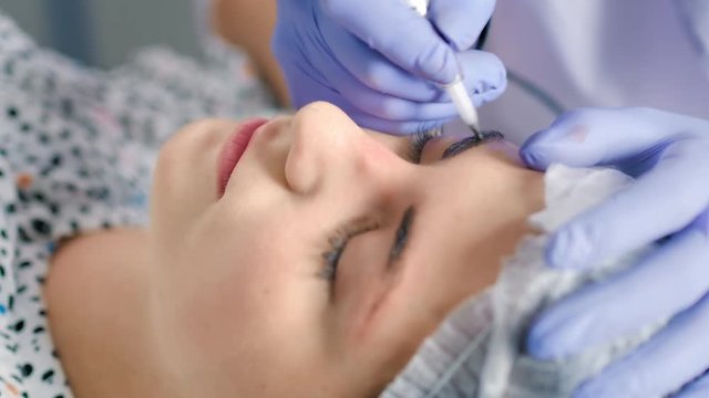 Close up cosmetologist making microblading procedure working with eyebrows