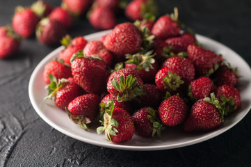 Fresh strawberries in a plate on a black background.